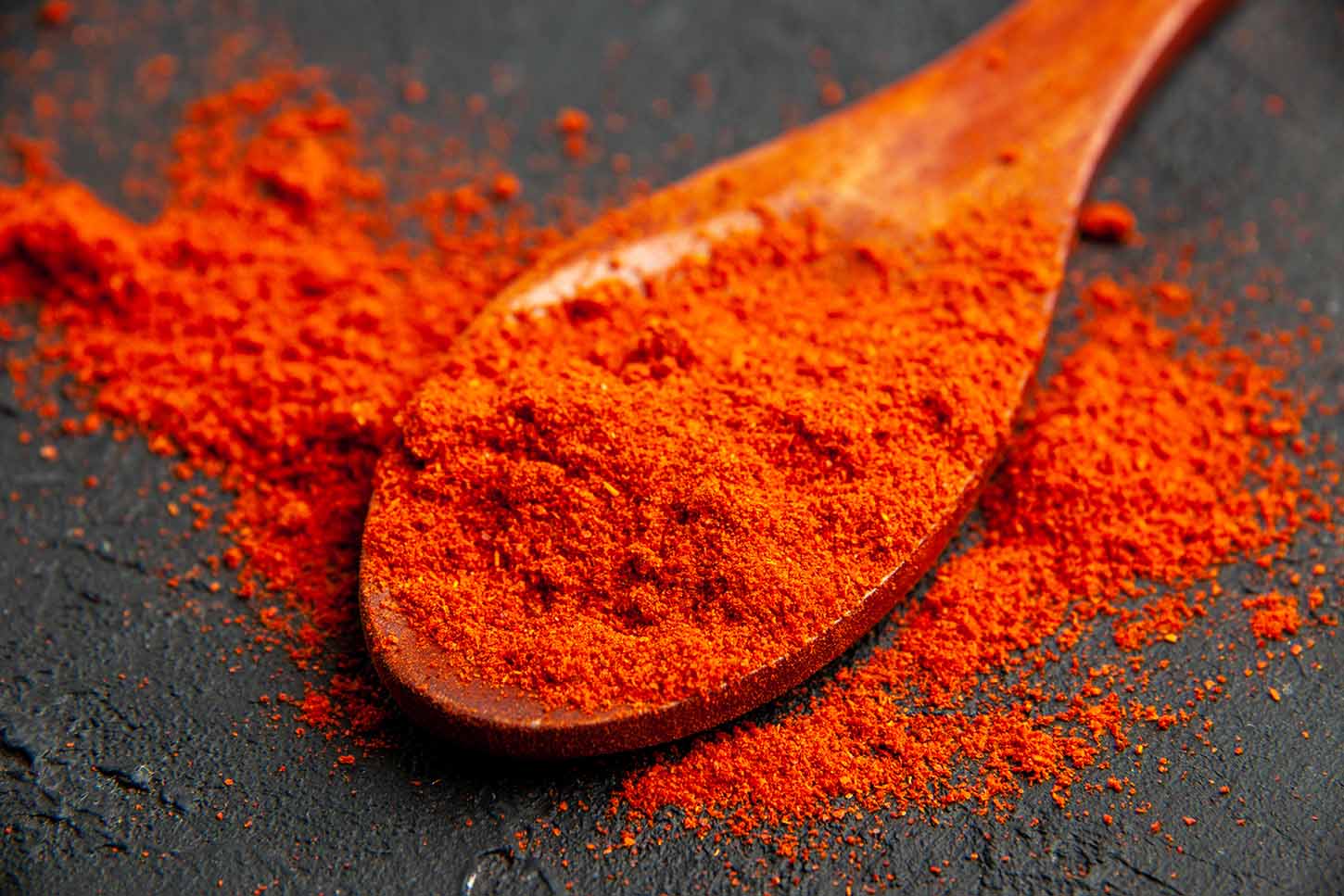 bottom view red pepper powder on wooden spoon on black table pimentón de la Vera Carlos demetrio